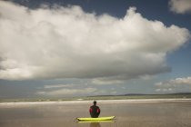 Вид сзади серфингиста, сидящего на доске для серфинга на пляже — стоковое фото