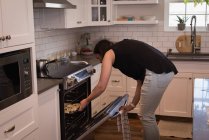 Woman putting patties inside oven in kitchen at home — Stock Photo