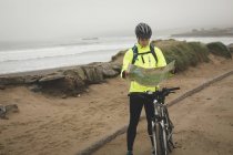 Young man with cycle reading map at the beach — Stock Photo