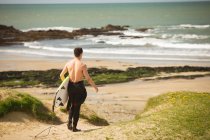 Vista posteriore del surfista con tavola da surf passeggiando sulla spiaggia — Foto stock