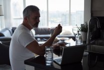 Людина, маючи сніданок, під час використання ноутбука на дому — стокове фото