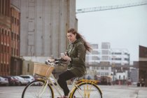 Beautiful woman using mobile phone while riding bicycle on street — Stock Photo