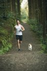 Ajuste homem correndo com seu cão na floresta exuberante — Fotografia de Stock