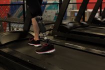 Sección baja de mujer madura haciendo ejercicio en la cinta de correr en el gimnasio - foto de stock