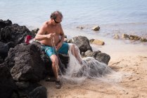 Fisherman holding fishing net on the beach — Stock Photo