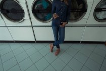 Baixa seção de mulher usando seu telefone enquanto espera na lavanderia — Fotografia de Stock