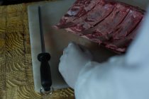 Средняя часть мясника режет мясо в мясной лавке — стоковое фото