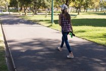 Вид ззаду жінки з навушниками і ковзанами, що ходять в парку — стокове фото
