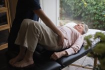 Fisioterapeuta dando un masaje corporal a una mujer mayor en casa - foto de stock