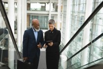 Geschäftsleute diskutieren auf einer Rolltreppe im Büro über ein Tablet — Stockfoto
