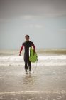 Surfista determinato con tavola da surf che corre sulla spiaggia — Foto stock