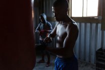 Jeune boxeur masculin attachant enveloppe à la main sur la main dans le studio de remise en forme — Photo de stock