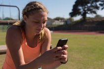 Sportlerin benutzte Handy am Sportplatz — Stockfoto