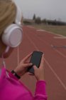 Atleta femenina escuchando música en el teléfono móvil en pista de atletismo - foto de stock