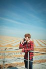 Мужчина, опирающийся на перила и использующий мобильный телефон в поле в солнечный день — стоковое фото