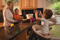 Girl taking photo of mother and baby in the kitchen at home — Stock Photo