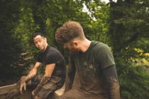 Ajuste los hombres que relajan sobre la carrera de obstáculos en el campo de entrenamiento - foto de stock