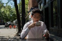 Молодий чоловік використовує мобільний телефон у відкритому кафе — стокове фото