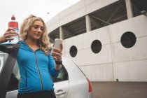 Красивая беременная женщина с помощью мобильного телефона на парковке — стоковое фото