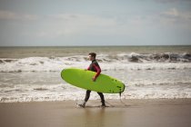 Vue latérale du surfeur avec planche de surf marchant sur la plage — Photo de stock