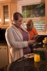 Мати з дитиною стоїть на кухні і використовує цифровий планшет вдома — стокове фото