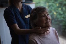 Fisioterapeuta dando un masaje en el cuello a una mujer mayor en casa - foto de stock
