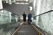 Homme d'affaires et femme d'affaires descendent sur un escalier roulant dans le bureau — Photo de stock