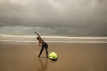 Vista traseira do surfista com prancha realizando exercício de alongamento na praia — Fotografia de Stock