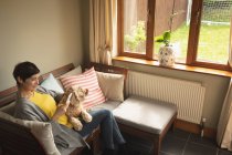 Женщина с помощью мобильного телефона с собакой на диване в гостиной на дому — стоковое фото