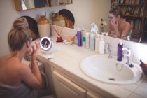 Женщина наносит крем для лица в ванной комнате дома — стоковое фото