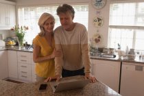 Усміхнена старша пара використовує ноутбук на кухні вдома — стокове фото