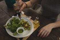 Молодая женщина наливает соевый соус на салат в кафе — стоковое фото
