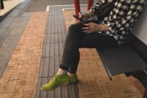 Низька частина молодої жінки, використовуючи мобільний телефон, сидить на лавці на тротуарі — стокове фото
