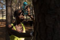 Atleta femenina con botella de agua tomando un descanso en el bosque - foto de stock