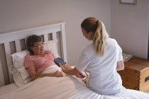 Physiothérapeute vérifiant la pression artérielle de la femme âgée à la maison — Photo de stock