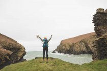 Vista posteriore di escursionista donna con braccia aperte in piedi sulla costa del mare — Foto stock
