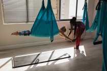 Female trainer assisting woman to exercise on swing sling hammock at fitness studio — Stock Photo