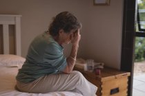 Mujer mayor preocupada sentada en la cama en casa - foto de stock