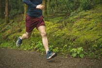 Baixa seção de homem correndo na floresta exuberante — Fotografia de Stock