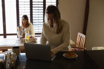 Lesbian couple using laptop while having coffee in kitchen at home — Stock Photo