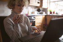 Молода жінка використовує ноутбук, маючи каву вдома — стокове фото