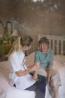 Physiotherapeut untersucht Seniorin zu Hause mit Stethoskop — Stockfoto