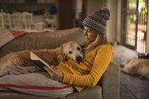 Menina com seu cão lendo um livro na sala de estar em casa — Fotografia de Stock