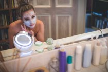 Mulher aplicando creme facial no banheiro em casa — Fotografia de Stock