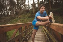 Молодий чоловік тягнеться на дерев'яний міст у лісі — стокове фото
