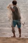 Vista traseira do pescador segurando rede de pesca na praia — Fotografia de Stock