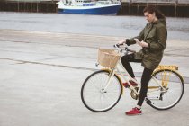 Mulher bonita na bicicleta usando telefone celular no porto — Fotografia de Stock
