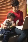 Primer plano madre e hijo sentado con un ordenador portátil en casa - foto de stock