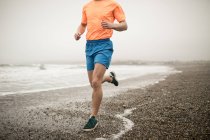 Low section of man jogging on shore at beach — Stock Photo
