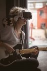 Молода жінка використовує віртуальну гарнітуру, граючи на гітарі вдома — стокове фото